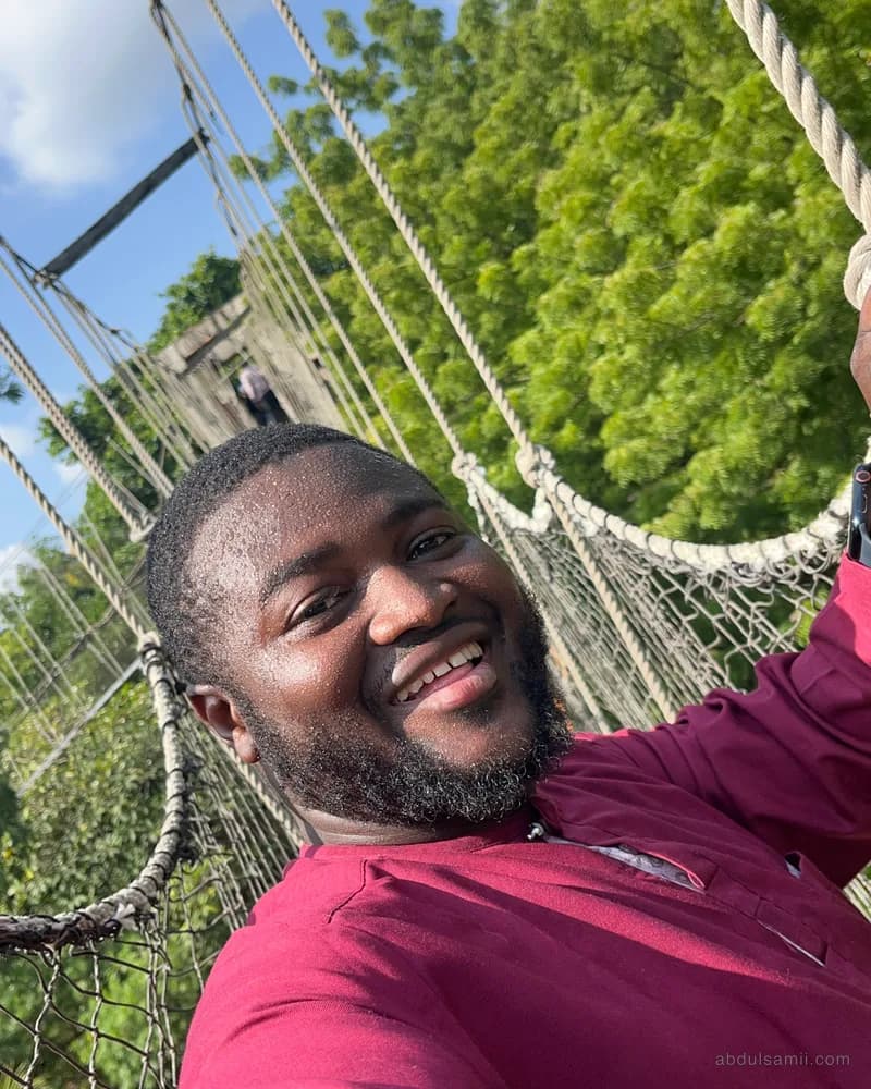 Abdulsamii smiling on a rope canopy walk among trees