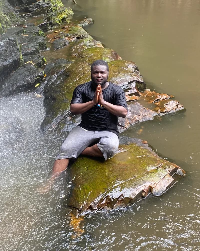 Abdulsamii sitting cross-legged on a rock in a river